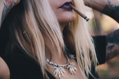 a blonde woman with dark lipstick and tattoos smokes a blunt