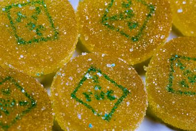 Yellow gummies with a green diamond with the words THC and exclamation mark in the middle. 