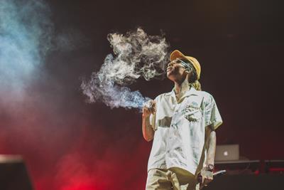 man on stage smoking a joint and blowing puffs of smoke into the air